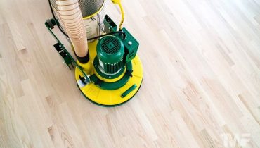 En profesjonell gulvslipemaskin sliper et lyst tregulv.