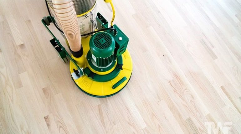 En profesjonell gulvslipemaskin sliper et lyst tregulv.